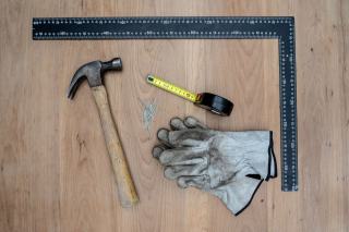 Marteau, équerre, mètre et gants posés sur un plateau en bois